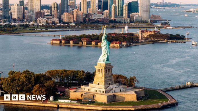 An aerial shot of Statue of Liberty and waters surrounding it with New York skyline in background